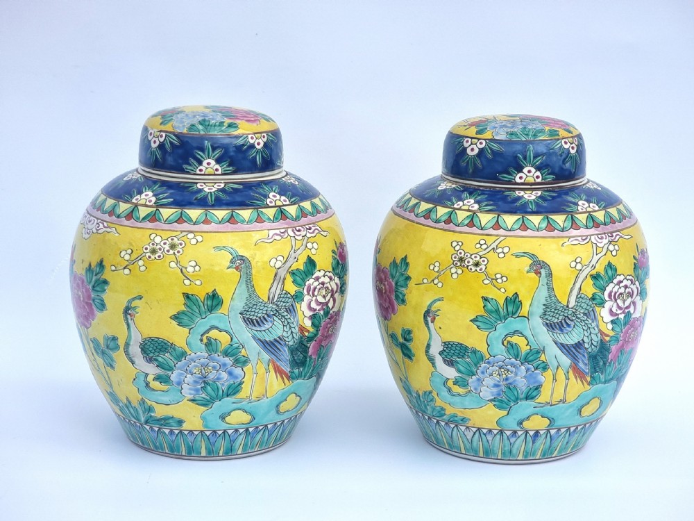 A matching pair of yellow porcelain ginger jars featuring hand-painted blue and turquoise phoenixes among peonies and floral branches, topped with deep blue decorated lids.