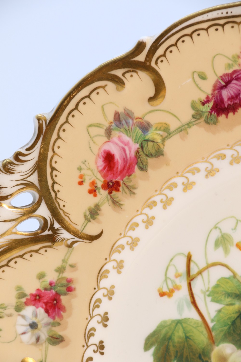 A cream-coloured circular porcelain cabinet plate featuring a scalloped gilded rim, floral swags, and a central hand-painted motif of a pineapple, grapes, and fruit. View VIII