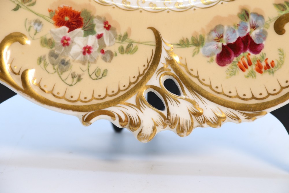 A cream-coloured circular porcelain cabinet plate featuring a scalloped gilded rim, floral swags, and a central hand-painted motif of a pineapple, grapes, and fruit. View XI