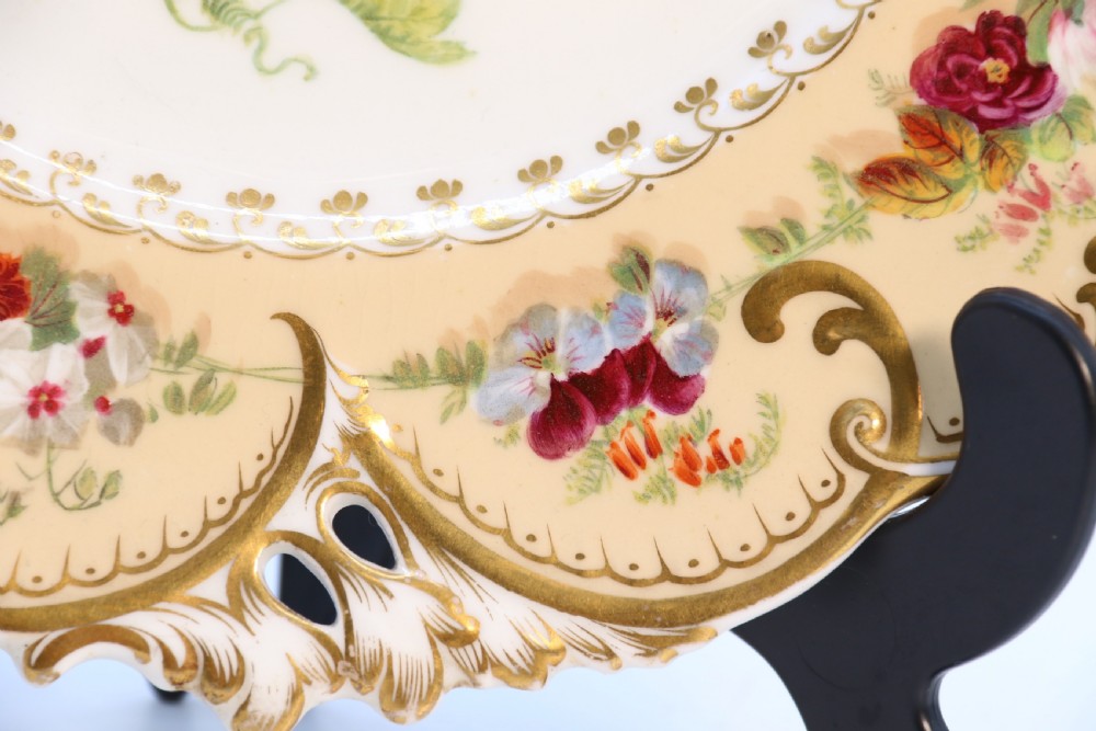 A cream-coloured circular porcelain cabinet plate featuring a scalloped gilded rim, floral swags, and a central hand-painted motif of a pineapple, grapes, and fruit. View XII
