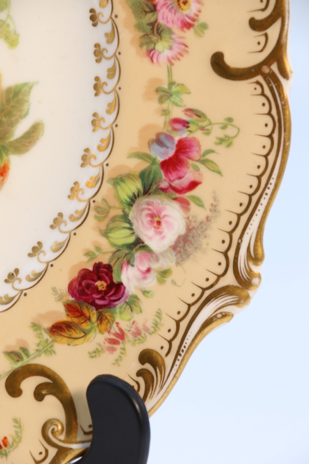 A cream-coloured circular porcelain cabinet plate featuring a scalloped gilded rim, floral swags, and a central hand-painted motif of a pineapple, grapes, and fruit. View XIII