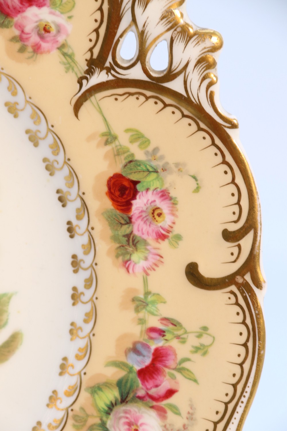A cream-coloured circular porcelain cabinet plate featuring a scalloped gilded rim, floral swags, and a central hand-painted motif of a pineapple, grapes, and fruit. View XIV