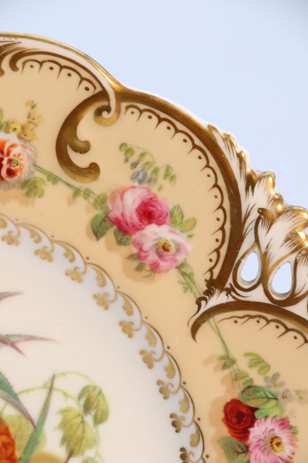 A cream-coloured circular porcelain cabinet plate featuring a scalloped gilded rim, floral swags, and a central hand-painted motif of a pineapple, grapes, and fruit. View XV
