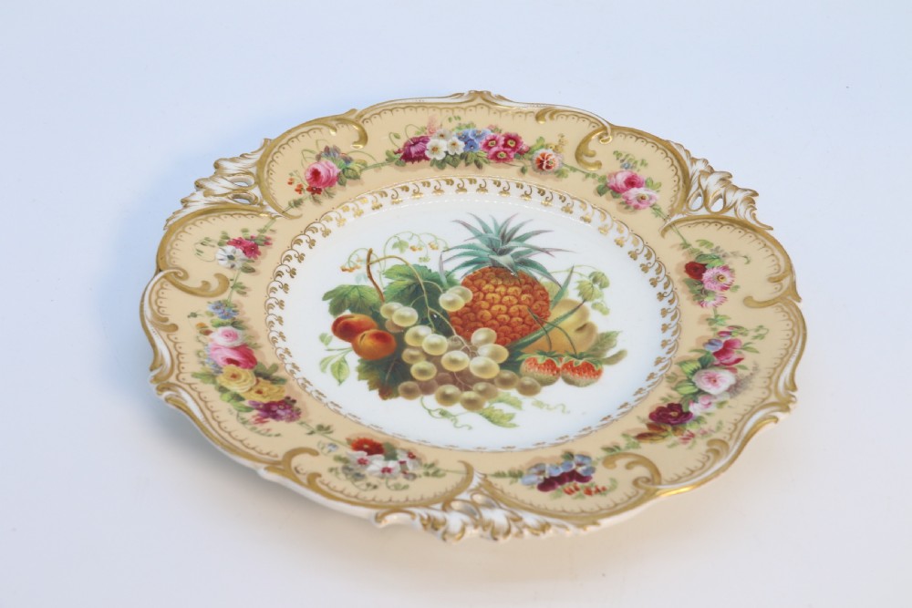 A cream-coloured circular porcelain cabinet plate featuring a scalloped gilded rim, floral swags, and a central hand-painted motif of a pineapple, grapes, and fruit. View XXIII