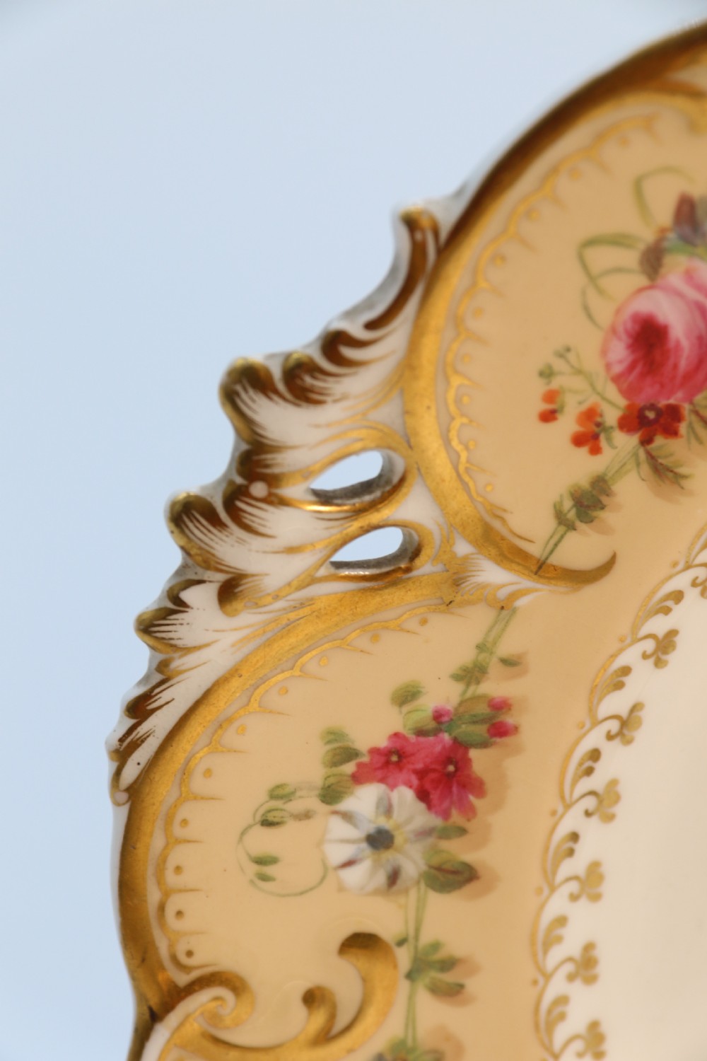 A cream-coloured circular porcelain cabinet plate featuring a scalloped gilded rim, floral swags, and a central hand-painted motif of a pineapple, grapes, and fruit. View XXV