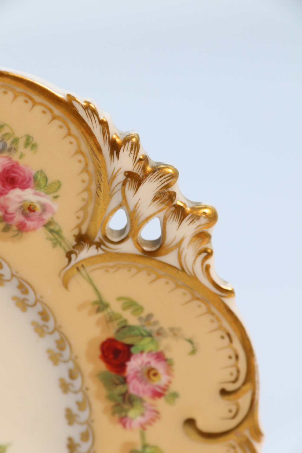 A cream-coloured circular porcelain cabinet plate featuring a scalloped gilded rim, floral swags, and a central hand-painted motif of a pineapple, grapes, and fruit. View XXVI