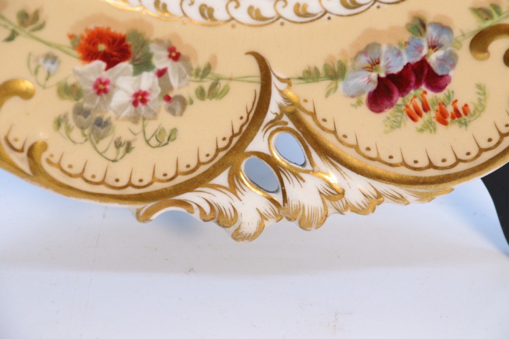 A cream-coloured circular porcelain cabinet plate featuring a scalloped gilded rim, floral swags, and a central hand-painted motif of a pineapple, grapes, and fruit. View XXVII