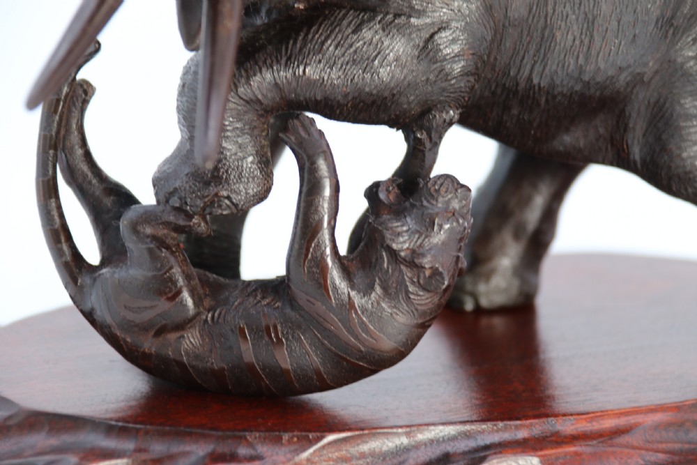 A dark patinated bronze sculpture depicting an elephant defending itself against two attacking tigers, mounted on a contoured wooden base. View VI