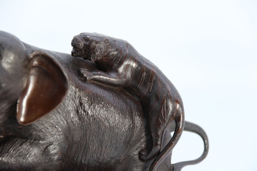 A dark patinated bronze sculpture depicting an elephant defending itself against two attacking tigers, mounted on a contoured wooden base. View VII