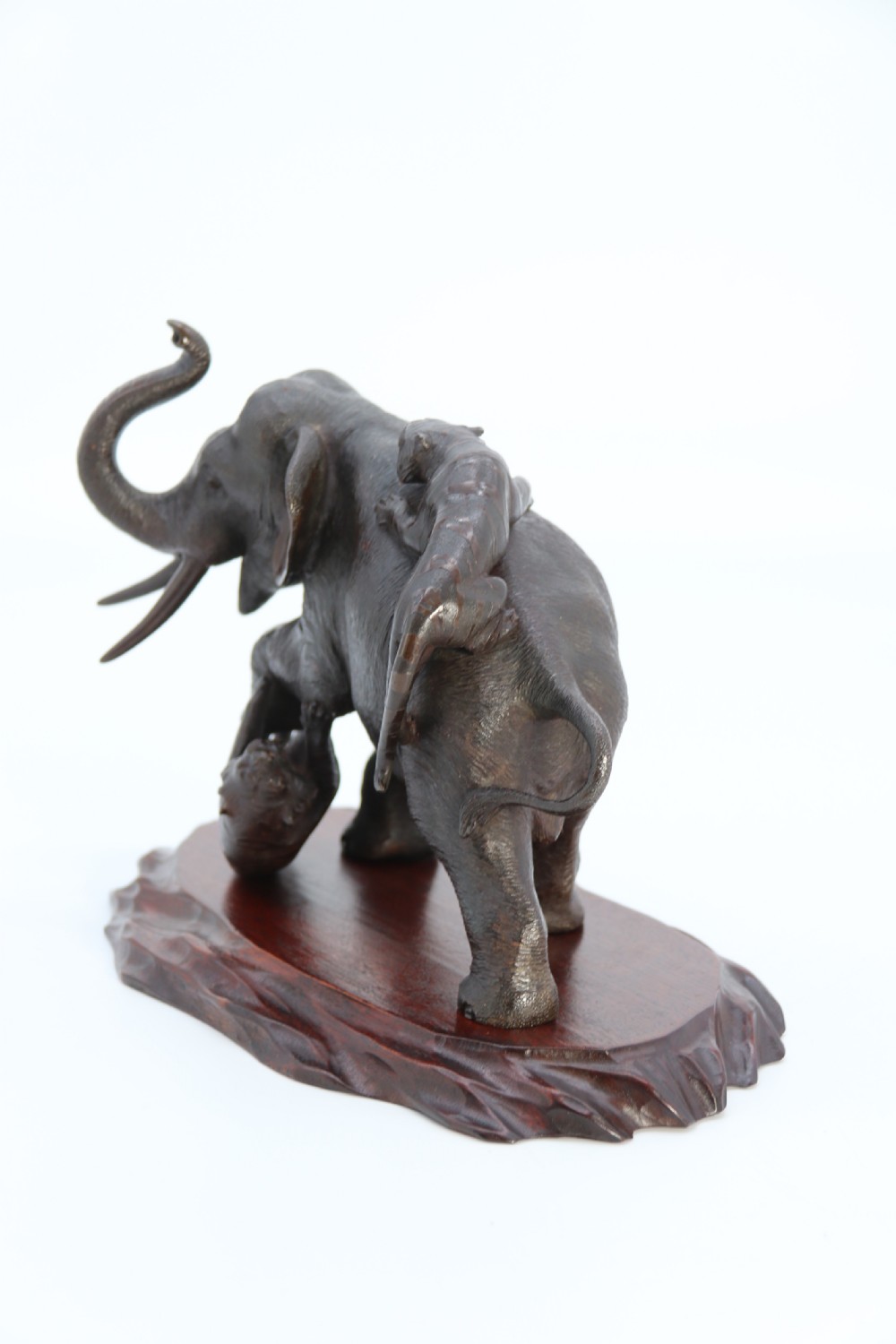 A dark patinated bronze sculpture depicting an elephant defending itself against two attacking tigers, mounted on a contoured wooden base. View VIII