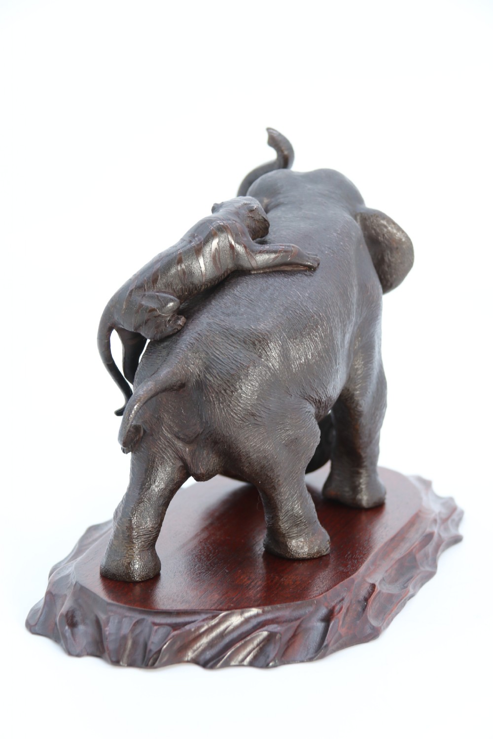 A dark patinated bronze sculpture depicting an elephant defending itself against two attacking tigers, mounted on a contoured wooden base. View XII