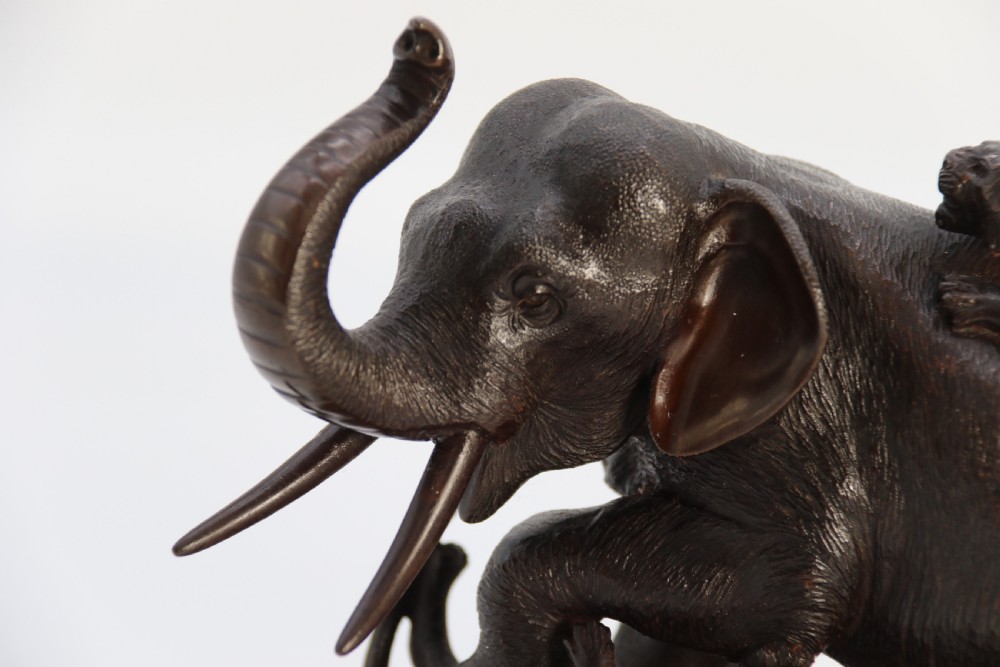 A dark patinated bronze sculpture depicting an elephant defending itself against two attacking tigers, mounted on a contoured wooden base. View XIV