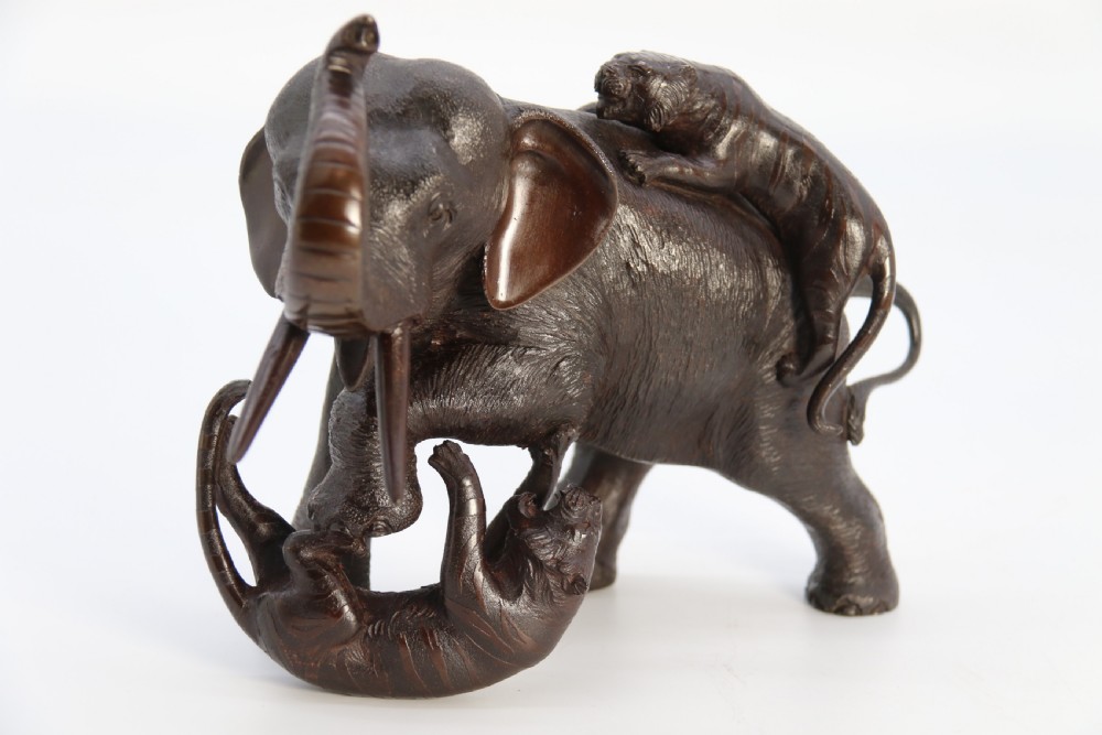 A dark patinated bronze sculpture depicting an elephant defending itself against two attacking tigers, mounted on a contoured wooden base. View XVIII