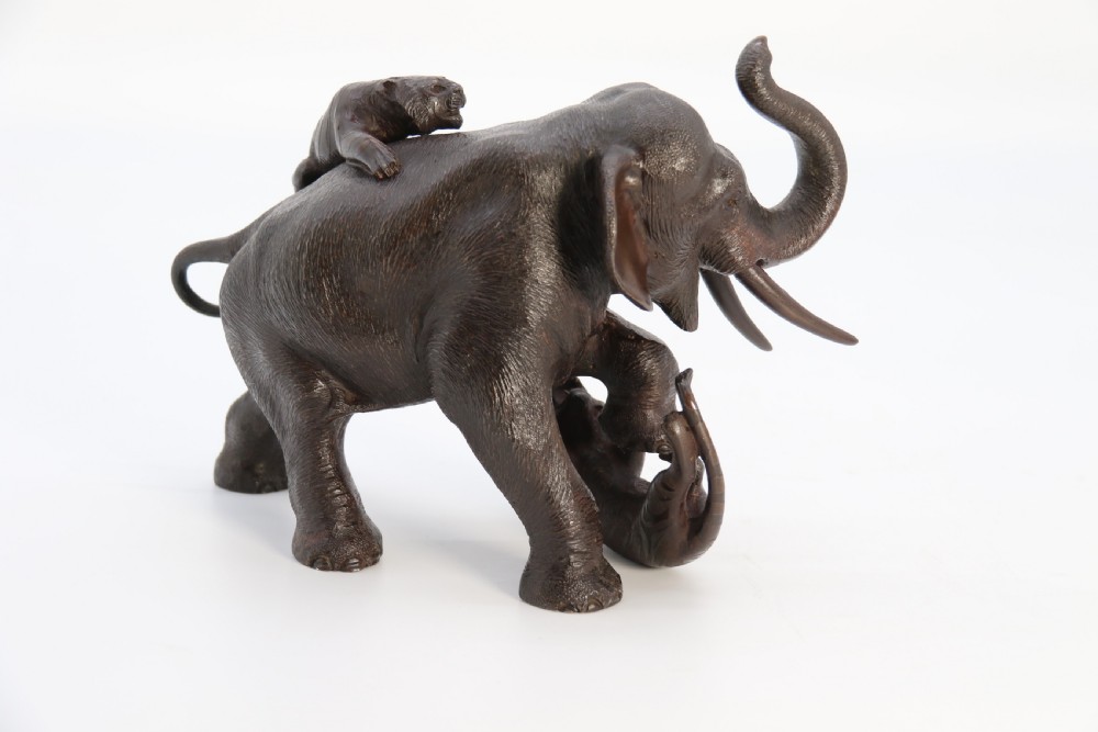A dark patinated bronze sculpture depicting an elephant defending itself against two attacking tigers, mounted on a contoured wooden base. View XIX