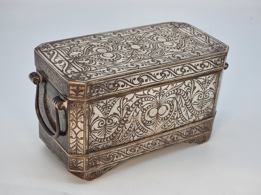 A rectangular dark bronze box featuring elaborate silver scrollwork inlay, side carrying handles, and small bracket feet.