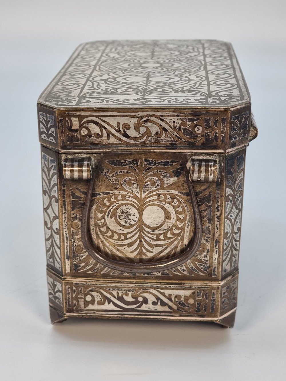A rectangular dark bronze box featuring elaborate silver scrollwork inlay, side carrying handles, and small bracket feet. View II