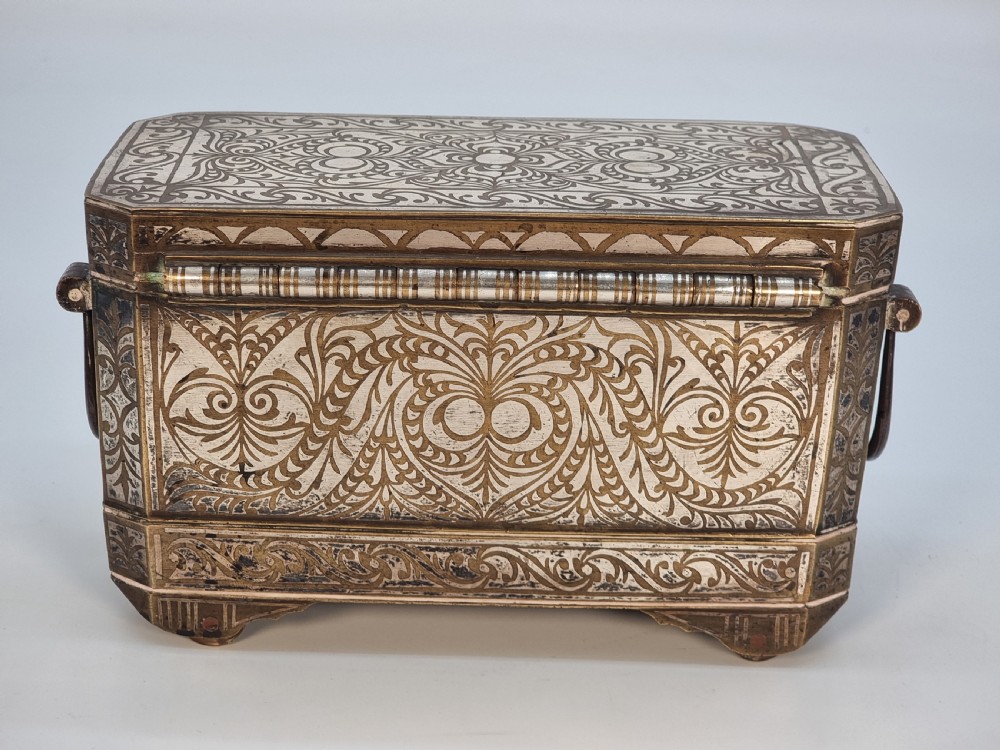 A rectangular dark bronze box featuring elaborate silver scrollwork inlay, side carrying handles, and small bracket feet. View IV