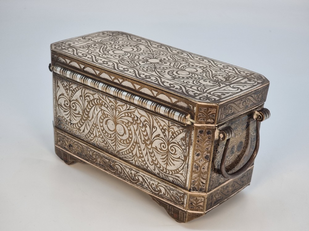 A rectangular dark bronze box featuring elaborate silver scrollwork inlay, side carrying handles, and small bracket feet. View V