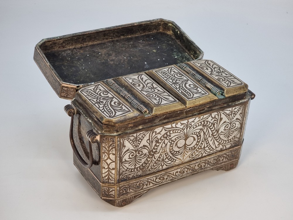 A rectangular dark bronze box featuring elaborate silver scrollwork inlay, side carrying handles, and small bracket feet. View VII