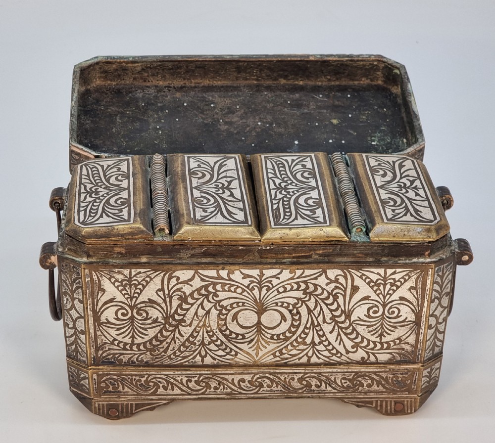 A rectangular dark bronze box featuring elaborate silver scrollwork inlay, side carrying handles, and small bracket feet. View VIII