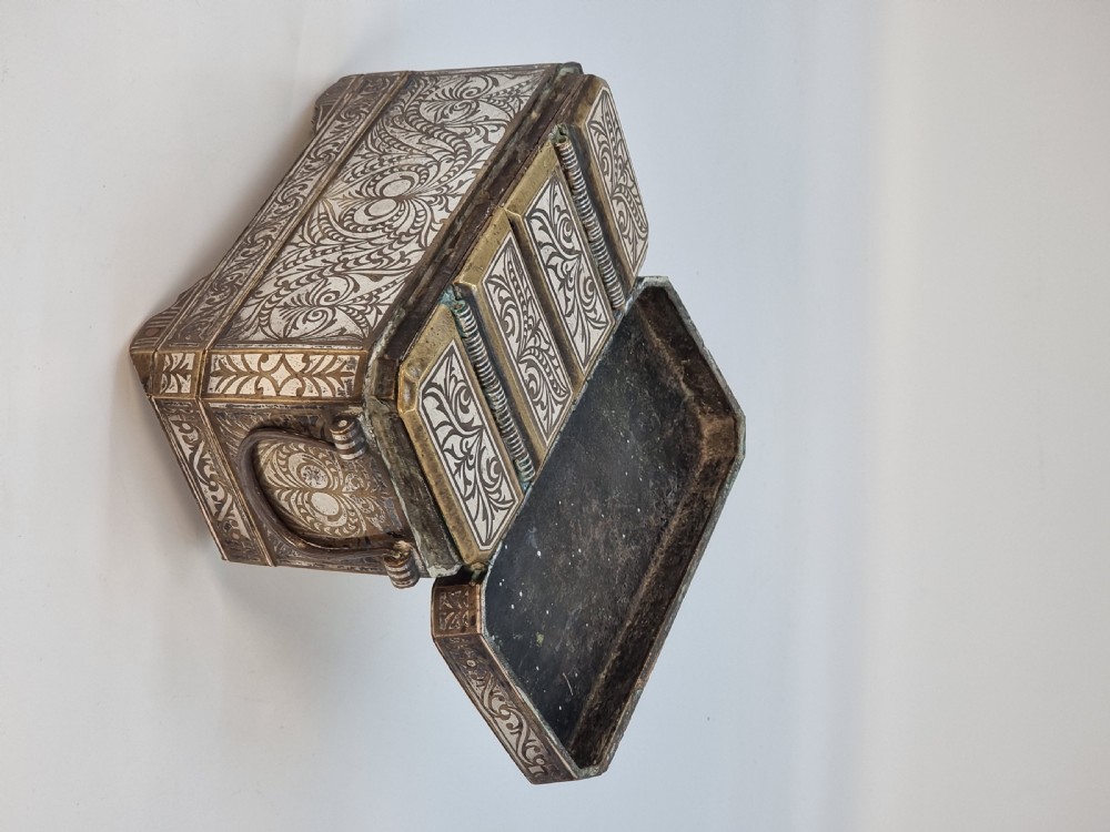 A rectangular dark bronze box featuring elaborate silver scrollwork inlay, side carrying handles, and small bracket feet. View X