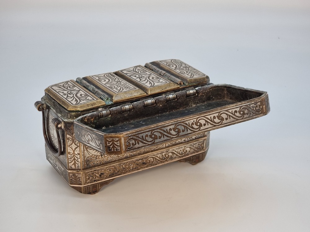 A rectangular dark bronze box featuring elaborate silver scrollwork inlay, side carrying handles, and small bracket feet. View XIII