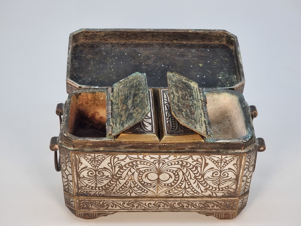 A rectangular dark bronze box featuring elaborate silver scrollwork inlay, side carrying handles, and small bracket feet. View XVI