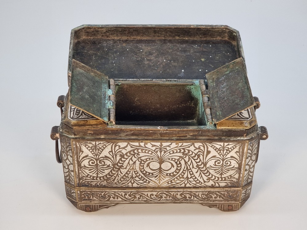 A rectangular dark bronze box featuring elaborate silver scrollwork inlay, side carrying handles, and small bracket feet. View XIX