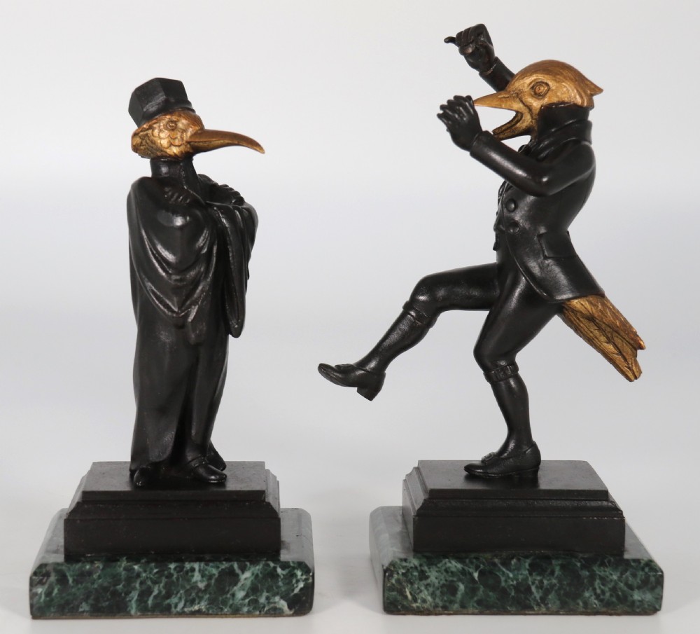 A pair of patinated and parcel-gilt bronze figures depicting anthropomorphic birds in nineteenth-century attire mounted on green marble bases.