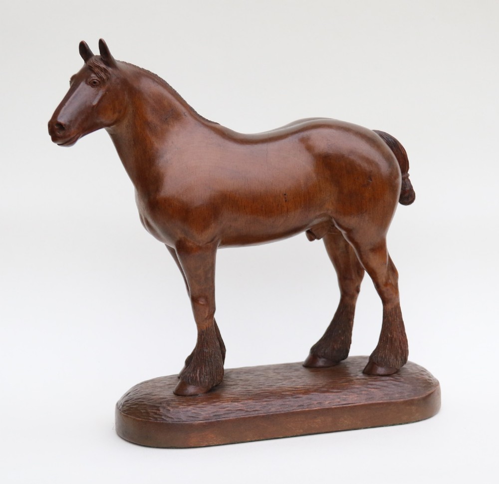 A hand-carved wooden sculpture depicting a Belgian draught horse stallion standing on an integral oval wood base.