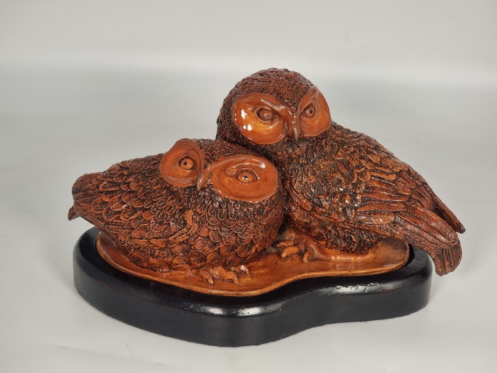 A hand-sculpted brown glazed pottery figurine of two owls perched together on a black ebonised wooden base. View III