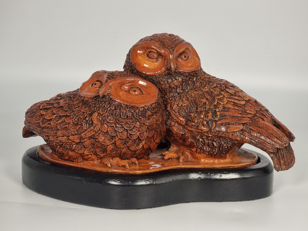 A hand-sculpted brown glazed pottery figurine of two owls perched together on a black ebonised wooden base. View X