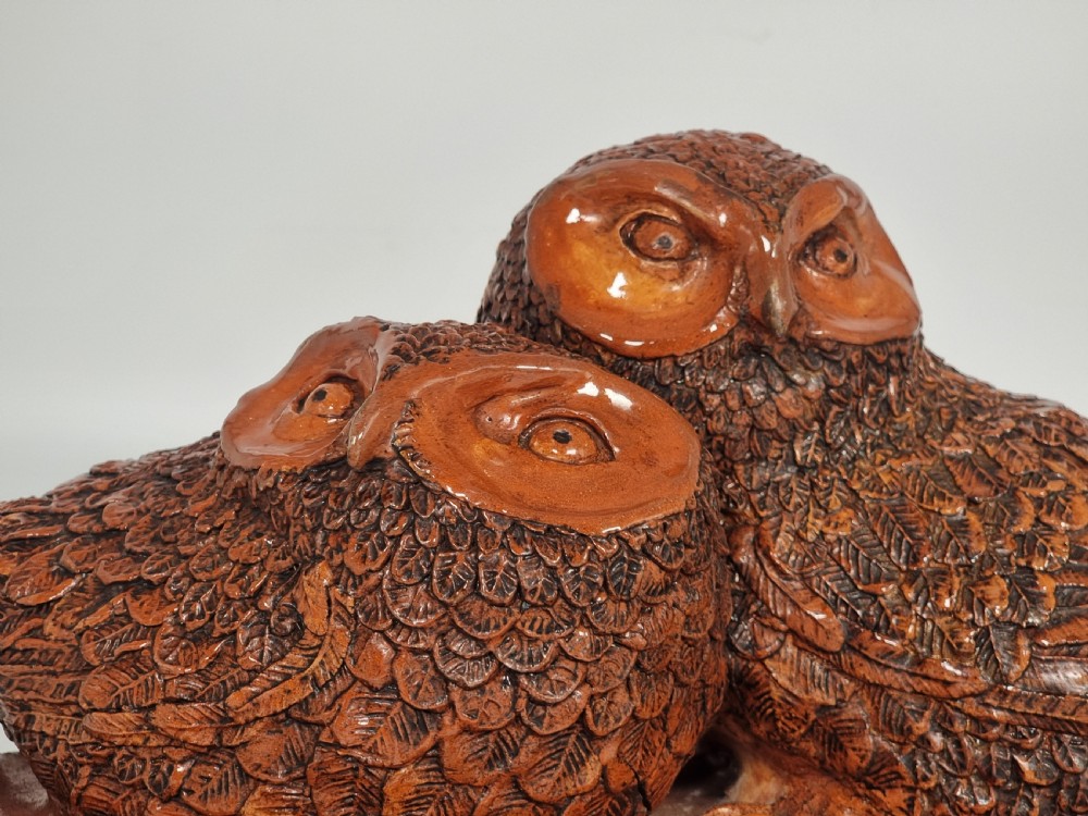 A hand-sculpted brown glazed pottery figurine of two owls perched together on a black ebonised wooden base. View XI