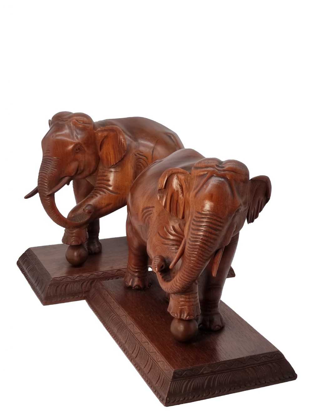 A pair of hand-carved warm brown teak wooden elephant sculptures balancing on balls mounted on rectangular bases.
