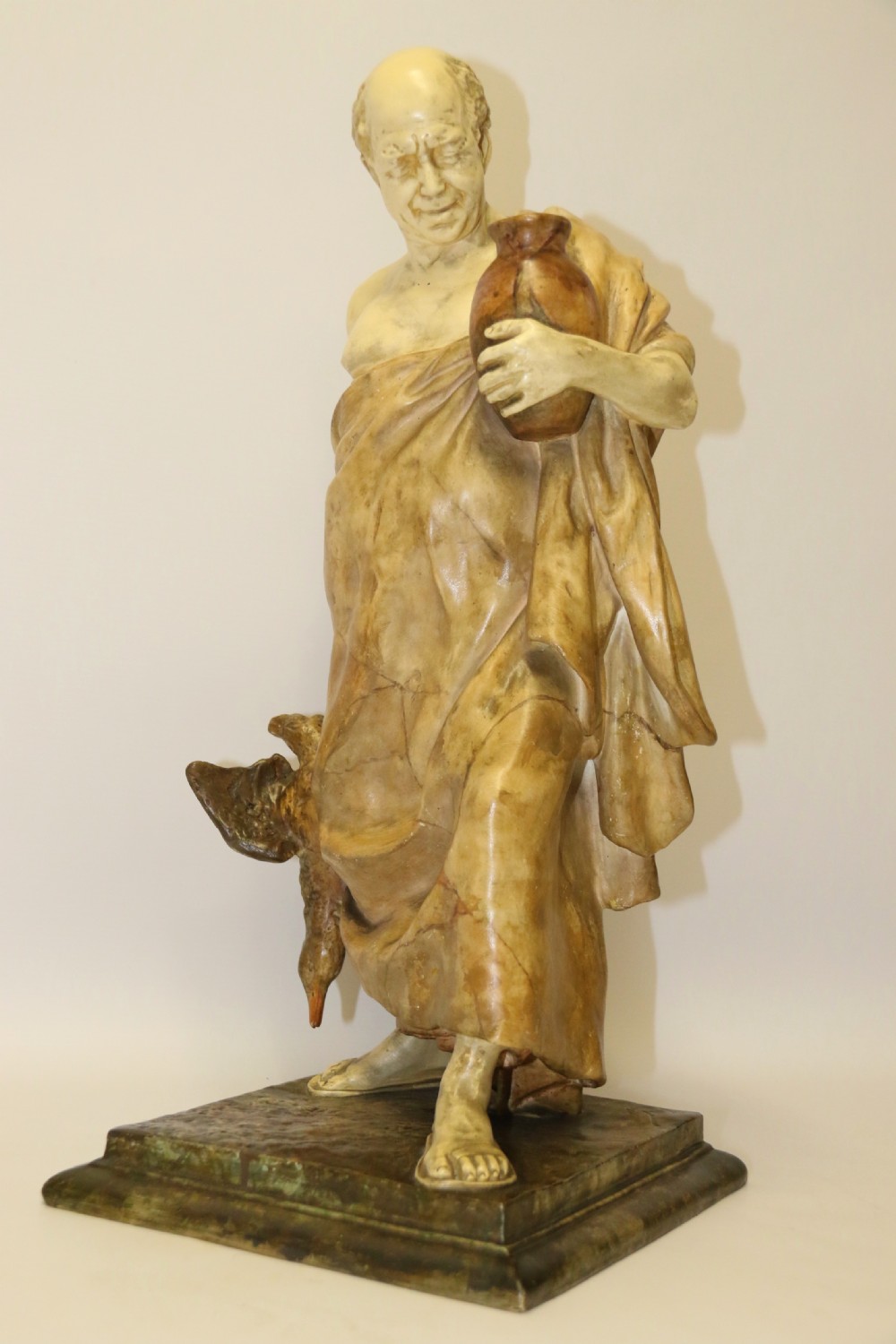 A 19th-century Goldscheider terracotta sculpture depicting a classical Roman male figure draped in robes, holding a vessel in one hand and a harvested bird in the other.