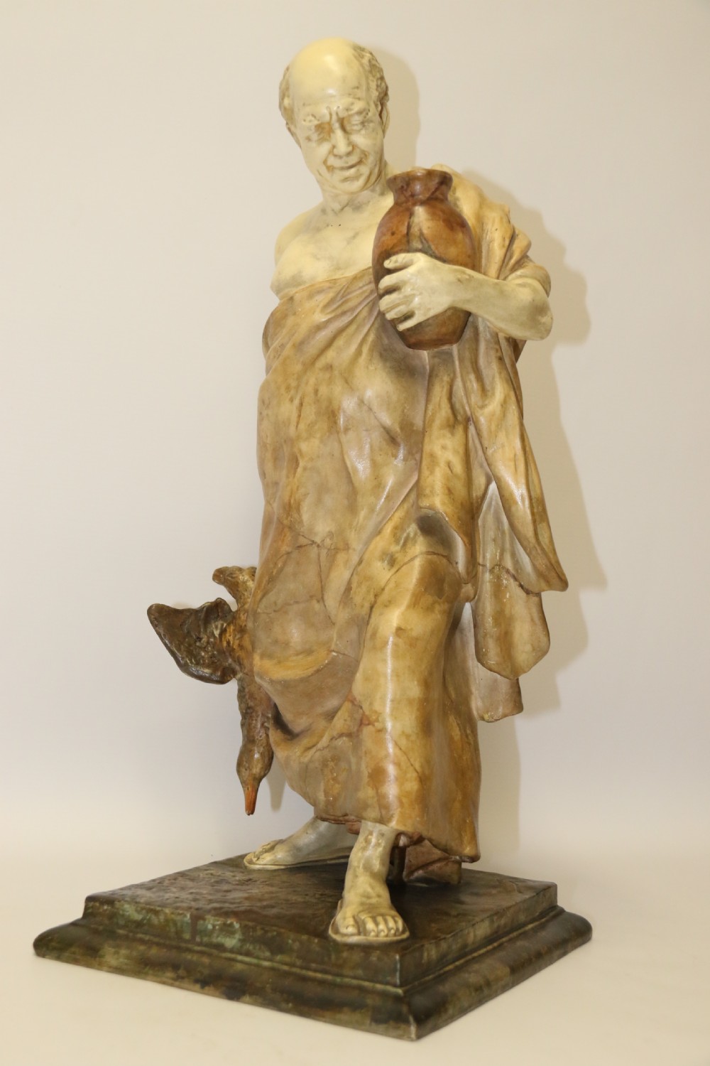 A 19th-century Goldscheider terracotta sculpture depicting a classical Roman male figure draped in robes, holding a vessel in one hand and a harvested bird in the other. View III