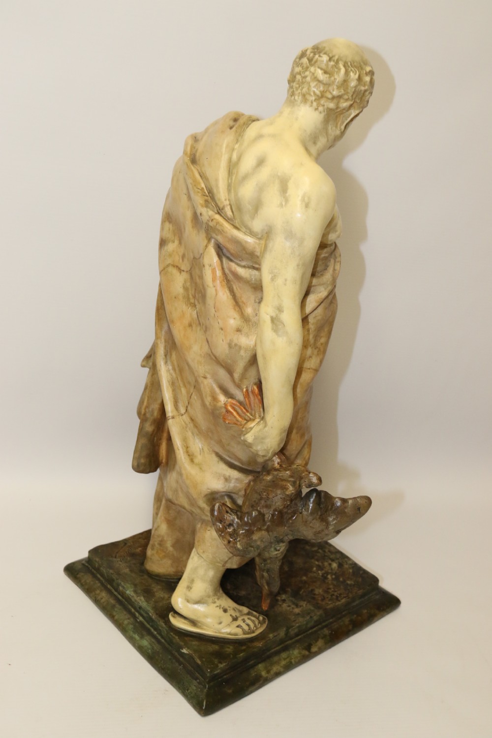 A 19th-century Goldscheider terracotta sculpture depicting a classical Roman male figure draped in robes, holding a vessel in one hand and a harvested bird in the other. View X