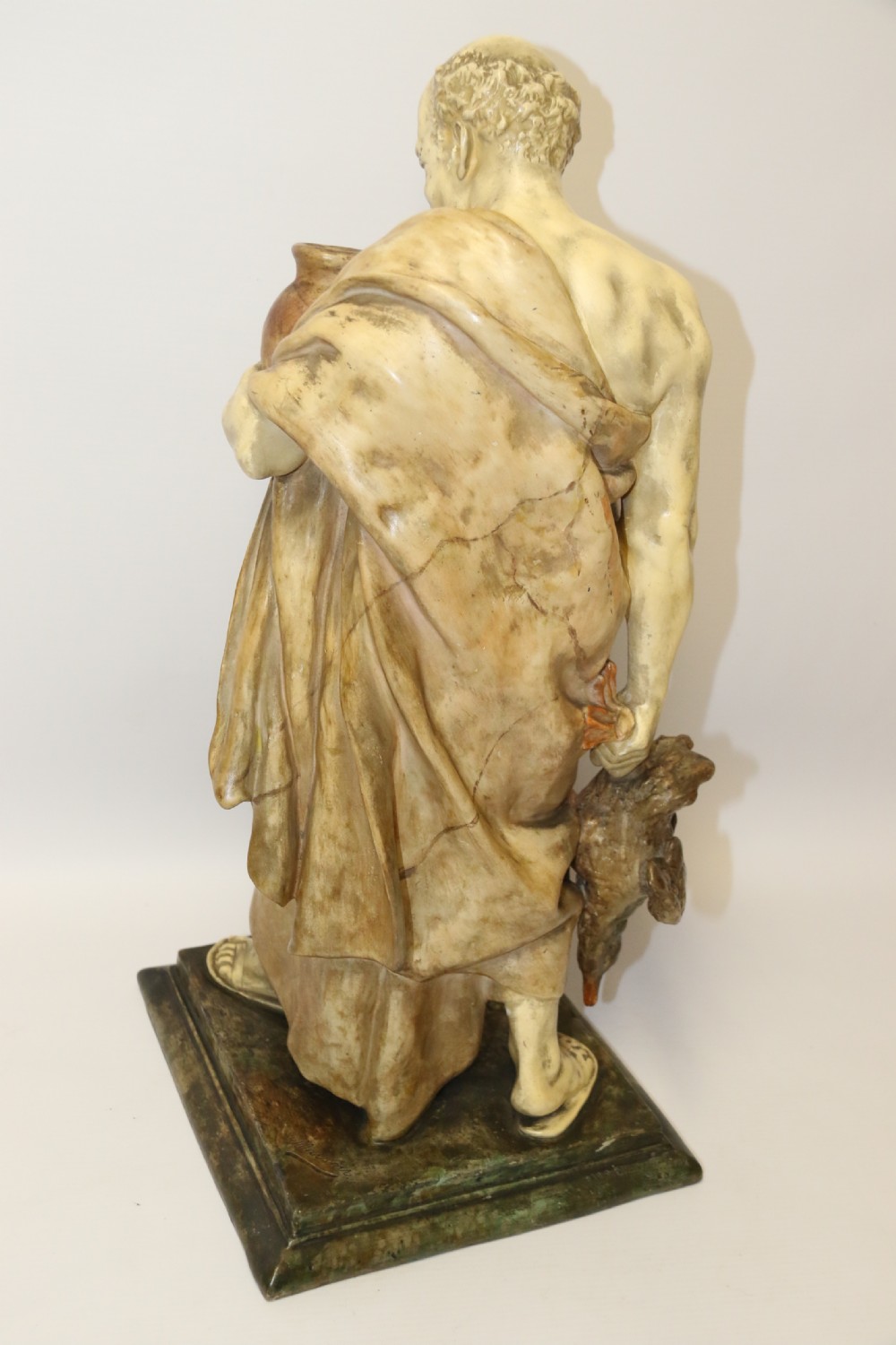 A 19th-century Goldscheider terracotta sculpture depicting a classical Roman male figure draped in robes, holding a vessel in one hand and a harvested bird in the other. View XI