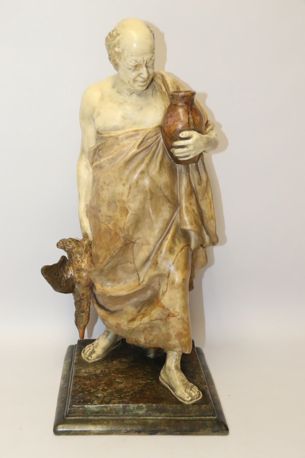 A 19th-century Goldscheider terracotta sculpture depicting a classical Roman male figure draped in robes, holding a vessel in one hand and a harvested bird in the other. View XIII