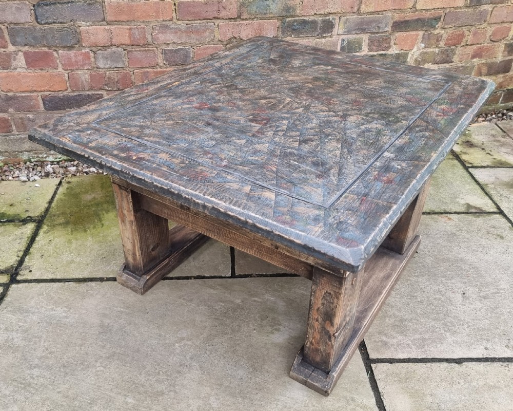 A low square rustic oak coffee table featuring a dark hand-painted geometric top and heavy timber legs. View X