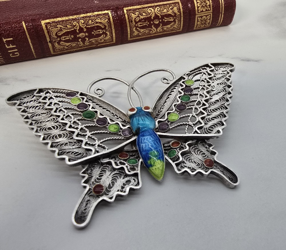 A silver filigree butterfly brooch featuring openwork wings filled with blue, green, purple, and red enamel details.
