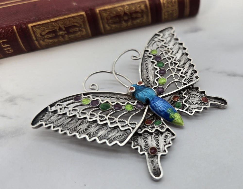 A silver filigree butterfly brooch featuring openwork wings filled with blue, green, purple, and red enamel details. View II