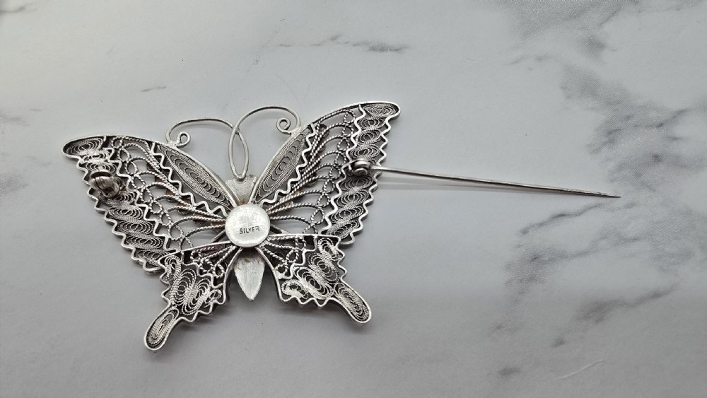 A silver filigree butterfly brooch featuring openwork wings filled with blue, green, purple, and red enamel details. View VII