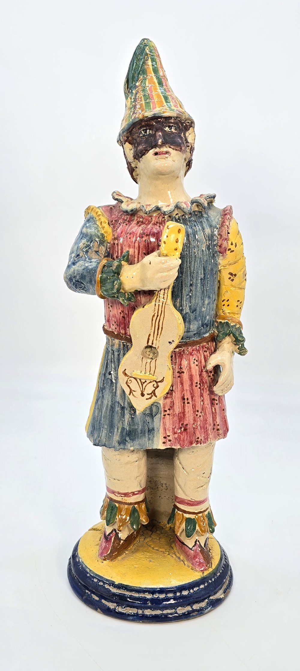 A polychrome glazed earthenware figure of a masked Commedia dellArte Pulcinella holding a stringed instrument.
