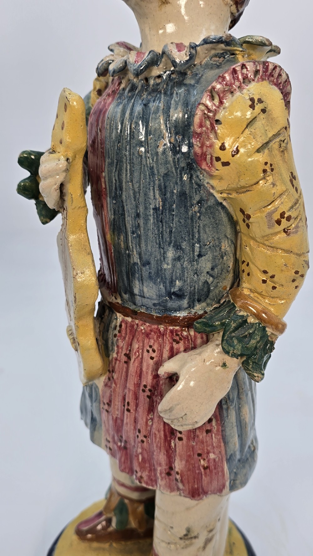 A polychrome glazed earthenware figure of a masked Commedia dellArte Pulcinella holding a stringed instrument. View XIV