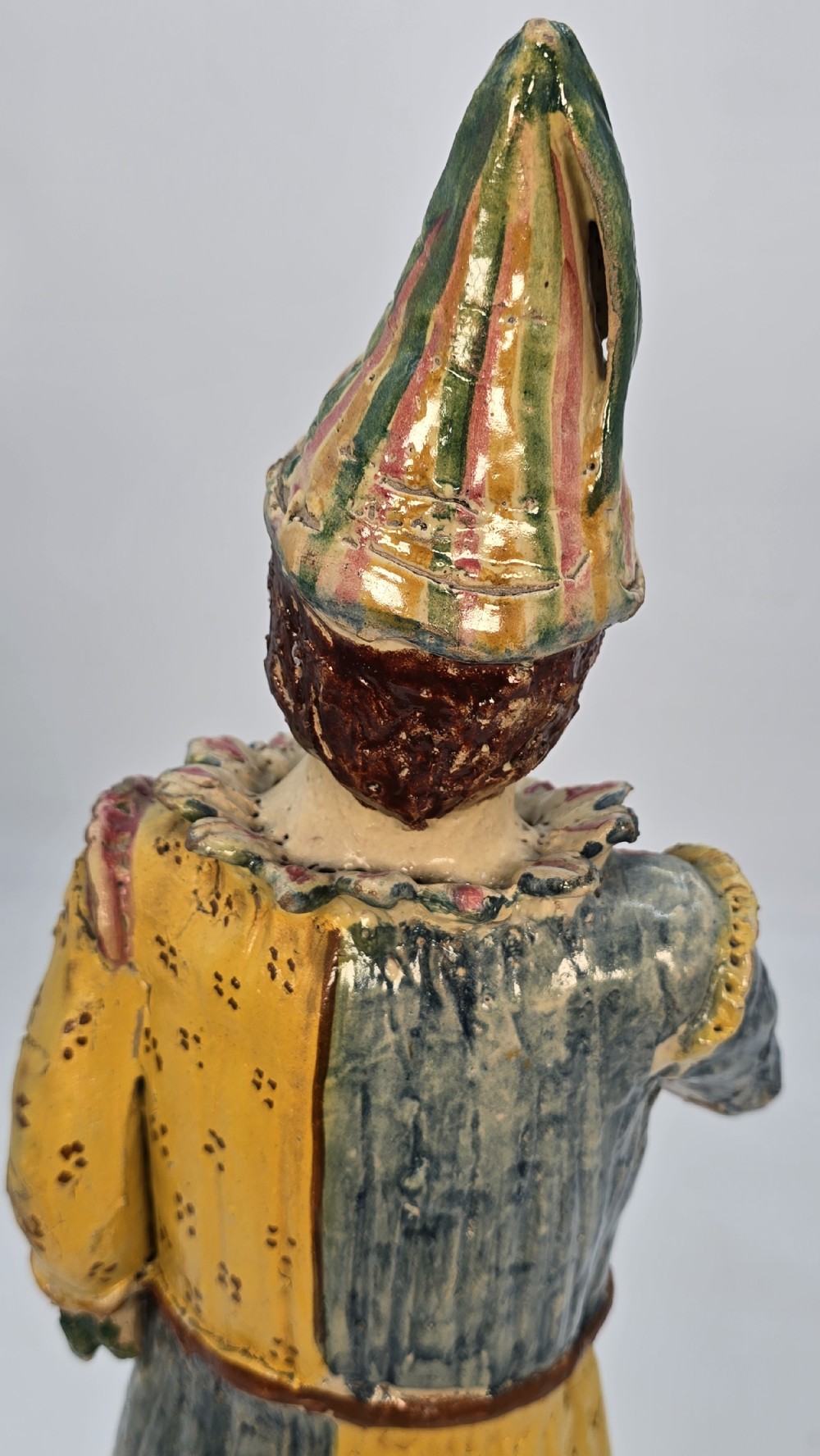 A polychrome glazed earthenware figure of a masked Commedia dellArte Pulcinella holding a stringed instrument. View XVI