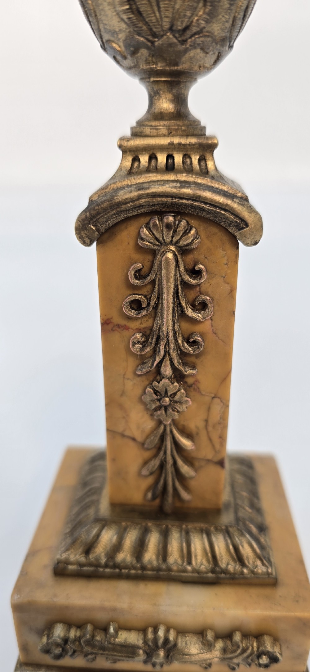 A pair of antique French Empire gilt bronze and yellow marble candlesticks featuring urn-shaped sconces, tapered rectangular pillars with floral appliques, and square bases on small ball feet. View XV