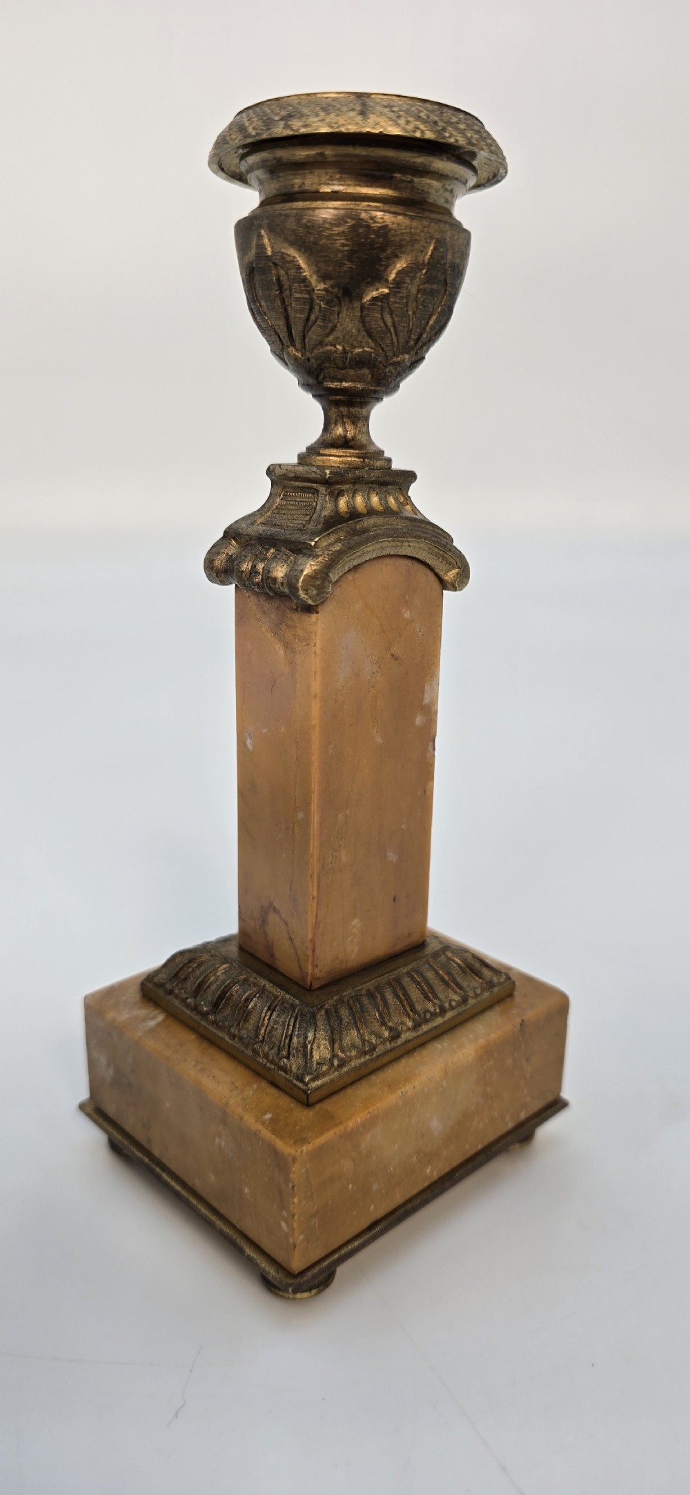 A pair of antique French Empire gilt bronze and yellow marble candlesticks featuring urn-shaped sconces, tapered rectangular pillars with floral appliques, and square bases on small ball feet. View XX