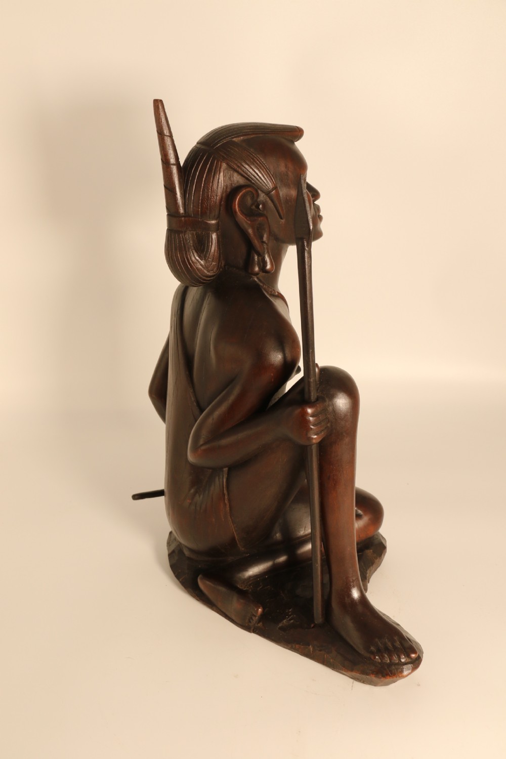 A dark hardwood hand-carved sculpture of a kneeling Maasai warrior holding a spear and club on an integrated wooden base. View III