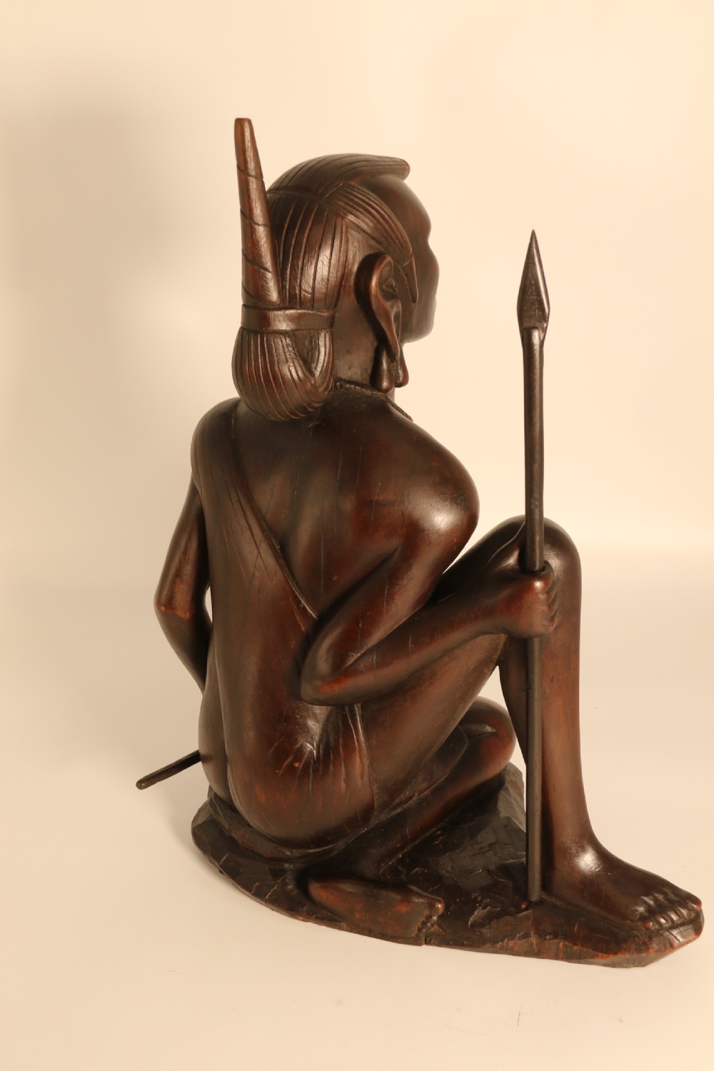 A dark hardwood hand-carved sculpture of a kneeling Maasai warrior holding a spear and club on an integrated wooden base. View IV